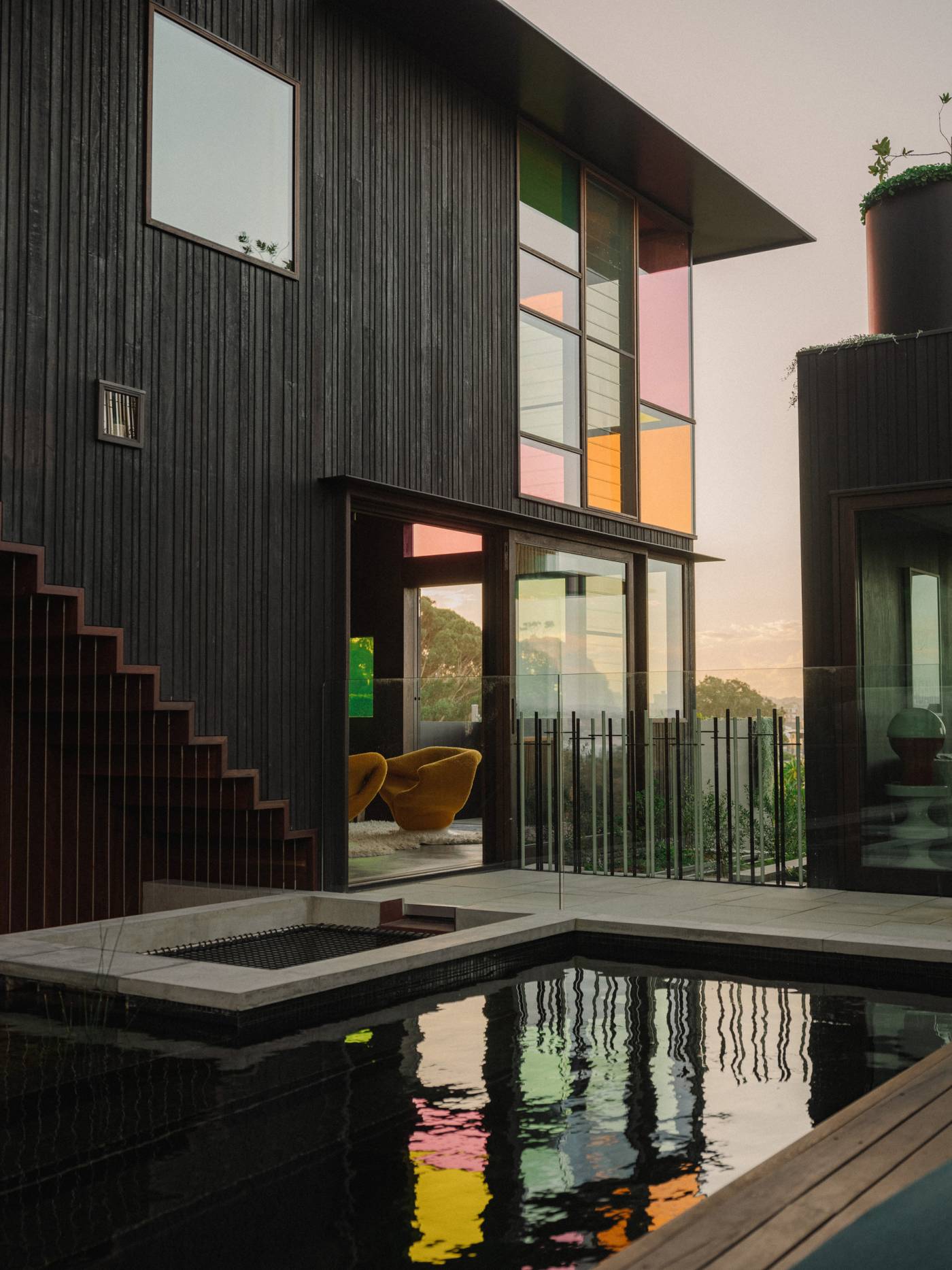 Dark timber-clad exterior of Holocene House in Sydney, with colourful upper windows overlooking the swimming pool.