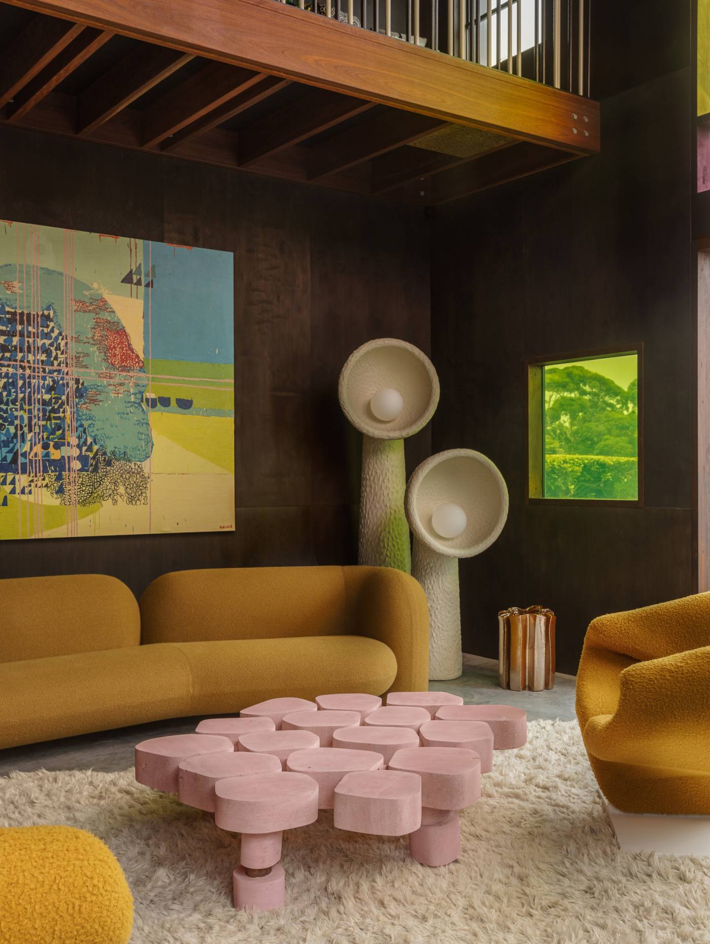 Gio sofa against a dark timber wall, accompanied by a pink coffee table and sculptural floor lamps.