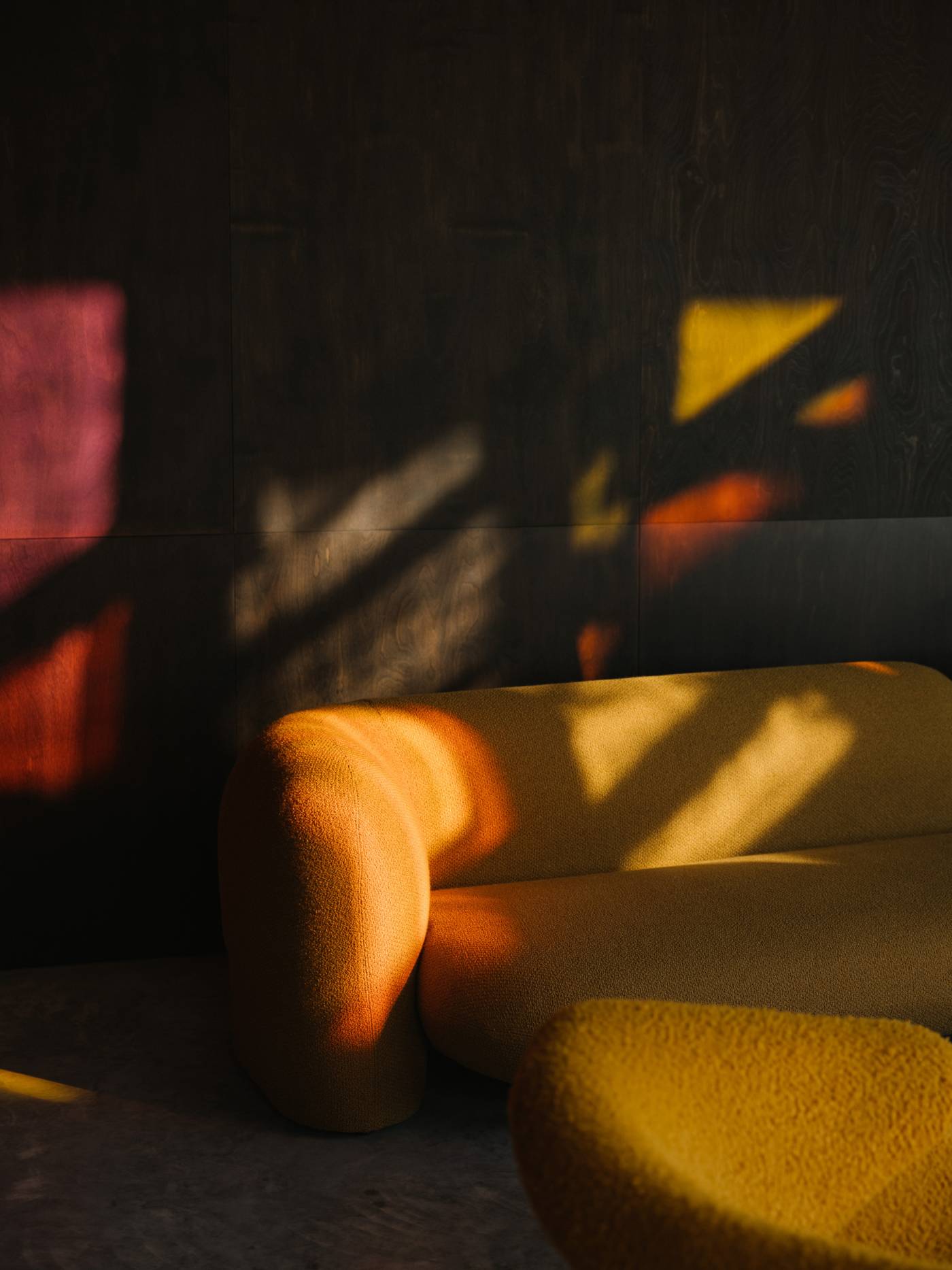 Close-up of the Gio sofa's curved armrest and ochre upholstery, illuminated by warm sunlight.