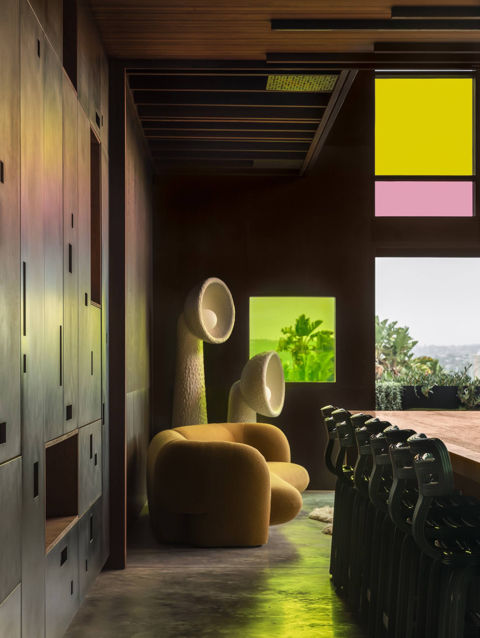 Rounded ochre upholstered seating beside two sculptural floor lamps in the timber-lined interior of Holocene House.